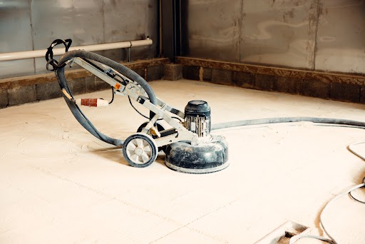 A floor cleaning machine sits on a dusty concrete surface, ready for floor tile restoration in an industrial space awaiting renewal.